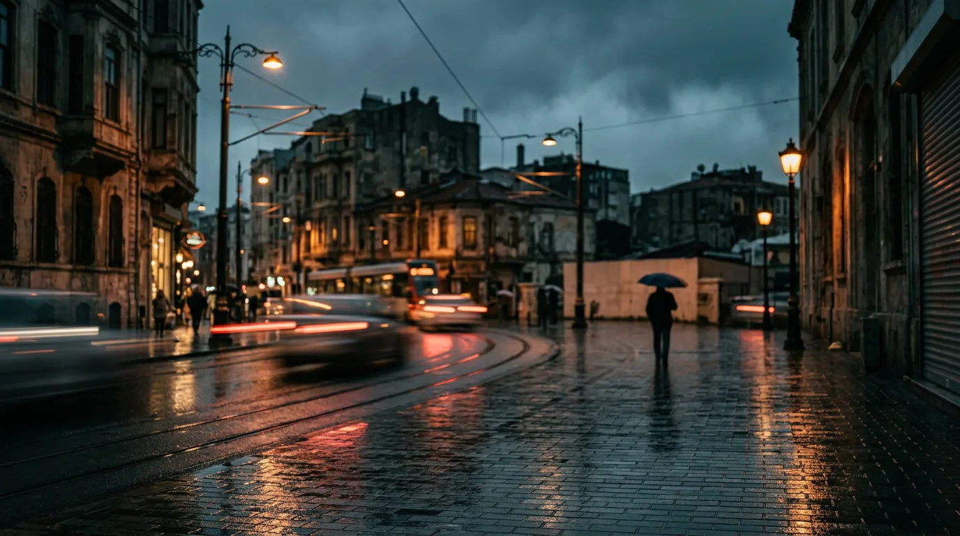Alacakaranlıkta ıslak İstanbul sokağında lamba ışıklarının yansımaları ve şemsiyeli tek bir silüet.